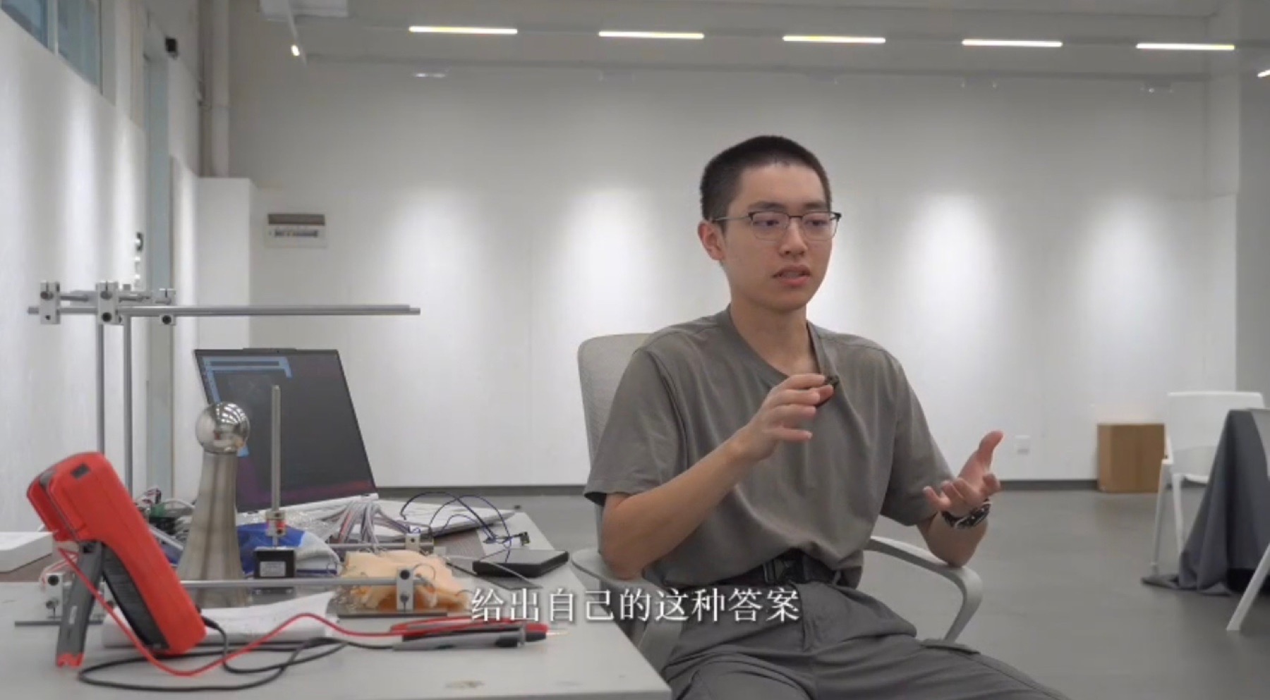 明亮工作室中，一位参与者坐在交互装置旁接受访谈，画面带有中文字幕